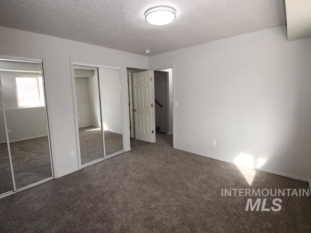 unfurnished bedroom with a textured ceiling, carpet flooring, and two closets