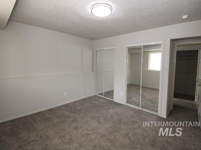 unfurnished bedroom featuring a textured ceiling, carpet floors, and multiple closets