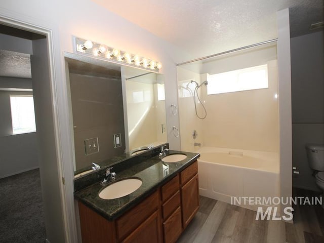 full bath with a sink, a textured ceiling, toilet, and wood finished floors