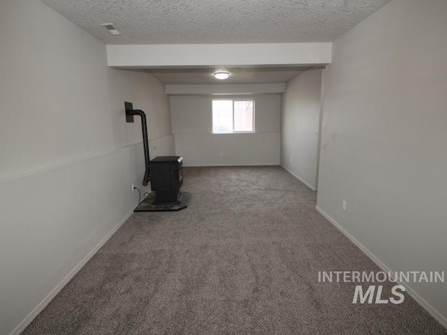 below grade area with a wood stove, carpet, visible vents, and a textured ceiling