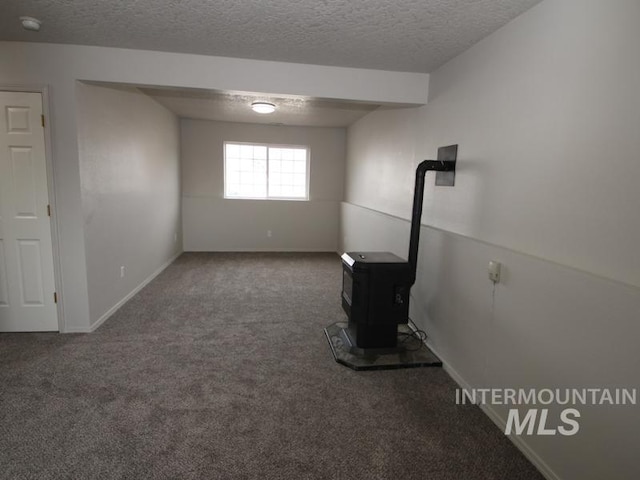 unfurnished living room with a wood stove, a textured ceiling, baseboards, and carpet flooring