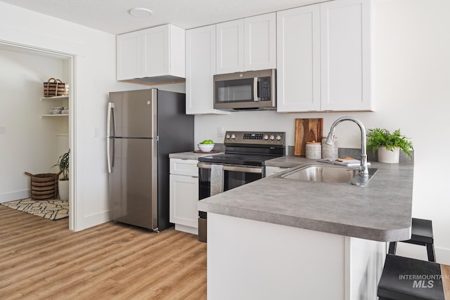 1371 SW Harrier Ave, Mountain Home, ID 83647 - kitchen featuring white cabinets, a peninsula, light wood finished floors, appliances with stainless steel finishes, and a sink