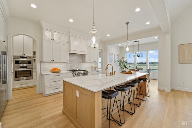 kitchen with custom range hood, a sink, appliances with stainless steel finishes, light wood finished floors, and decorative backsplash