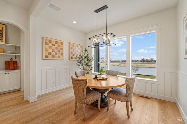 dining area featuring visible vents, a water view, light wood-style floors, and a wainscoted wall