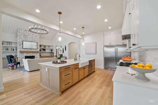 kitchen with a sink, stainless steel appliances, arched walkways, a stone fireplace, and light countertops