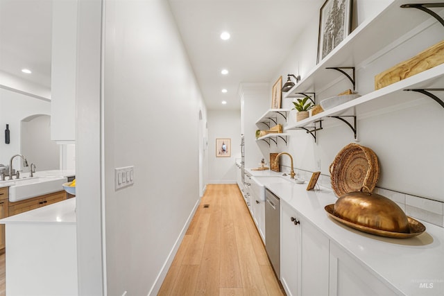 hallway featuring baseboards, recessed lighting, arched walkways, a sink, and light wood-style floors