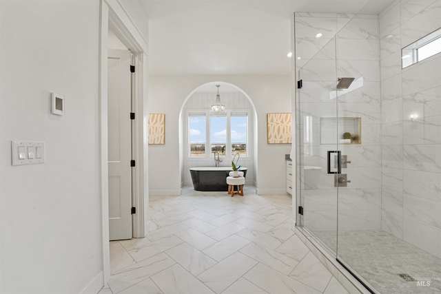 bathroom featuring marble finish floor, a freestanding bath, a shower stall, and baseboards