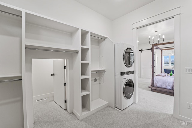 washroom featuring carpet, visible vents, stacked washing maching and dryer, a barn door, and a chandelier