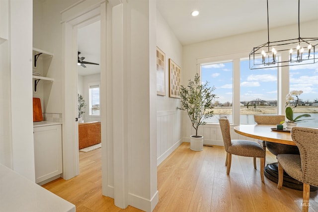 dining room with recessed lighting, wainscoting, a decorative wall, ceiling fan with notable chandelier, and light wood-type flooring