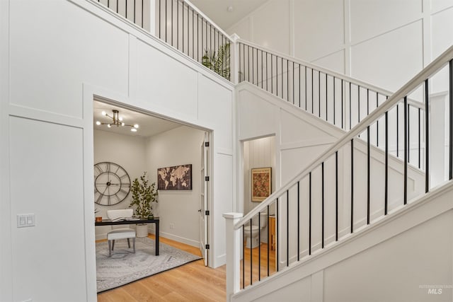 stairs featuring a high ceiling, an inviting chandelier, wood finished floors, and a decorative wall