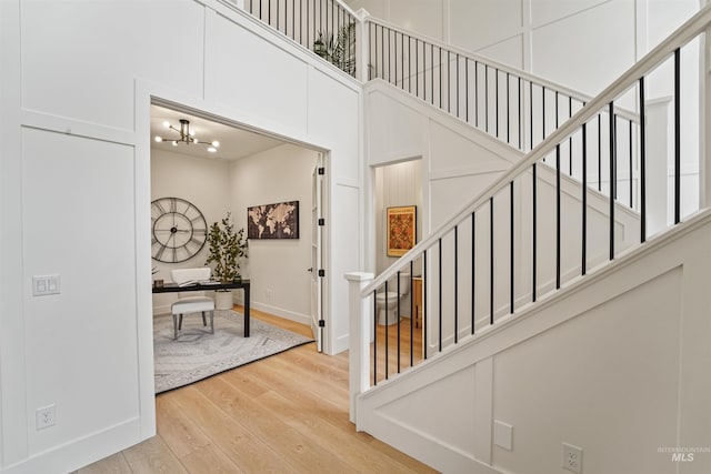 staircase with a chandelier, a towering ceiling, baseboards, and wood finished floors