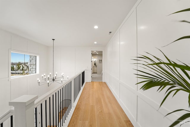 hallway featuring a decorative wall, recessed lighting, light wood-style floors, and an inviting chandelier