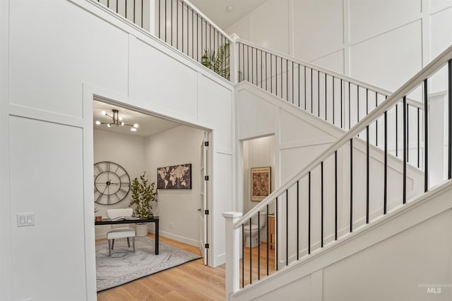 stairway featuring a notable chandelier, a decorative wall, a high ceiling, and wood finished floors