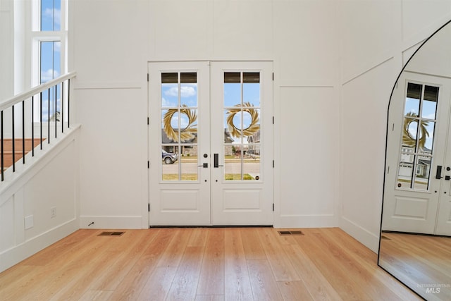 entrance foyer with a decorative wall, light wood-style floors, visible vents, and french doors