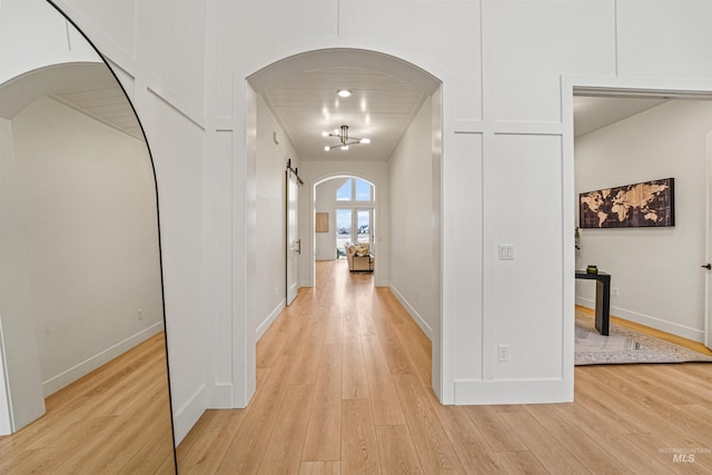 corridor with light wood-style flooring, baseboards, and arched walkways