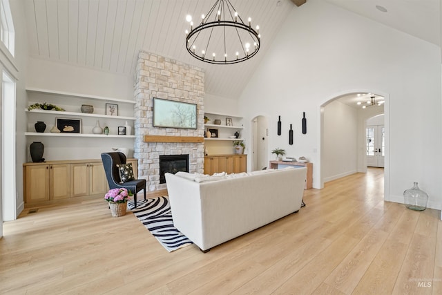 living area featuring light wood finished floors, built in shelves, a stone fireplace, an inviting chandelier, and arched walkways