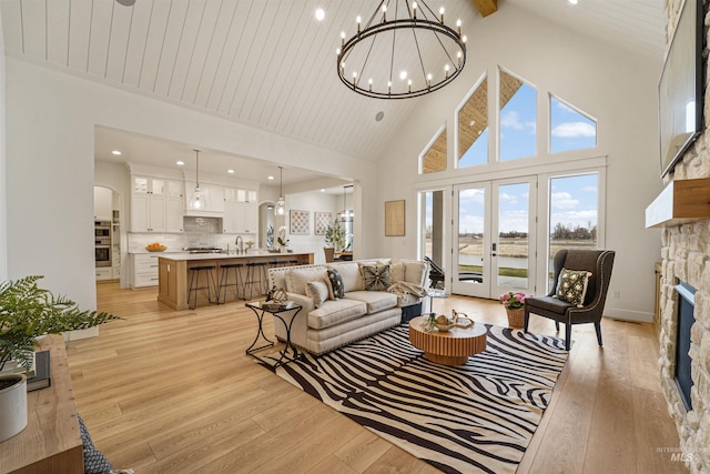 living area with light wood-type flooring, high vaulted ceiling, arched walkways, an inviting chandelier, and a fireplace