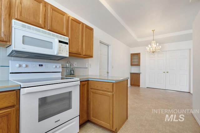 kitchen featuring pendant lighting, light countertops, a peninsula, an inviting chandelier, and white appliances