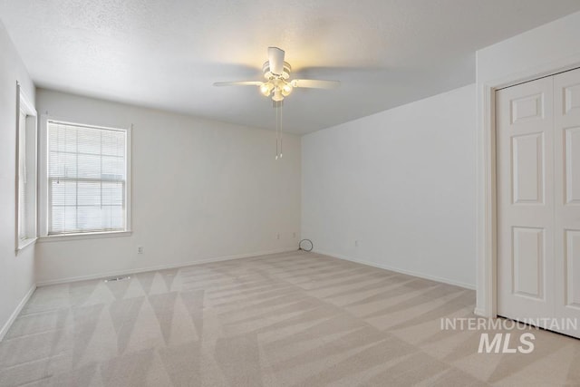empty room featuring baseboards, ceiling fan, and light colored carpet