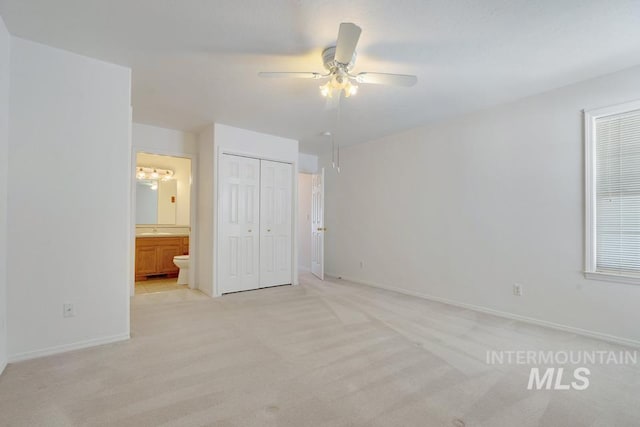 unfurnished bedroom featuring light colored carpet, connected bathroom, baseboards, and a closet