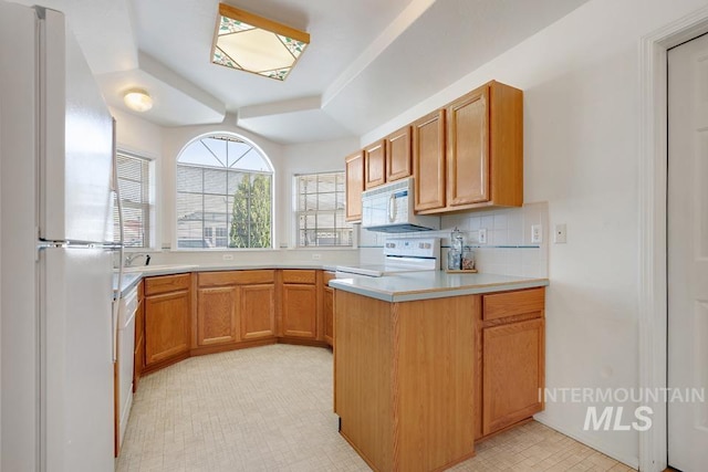 kitchen with light countertops, a peninsula, white appliances, and tasteful backsplash