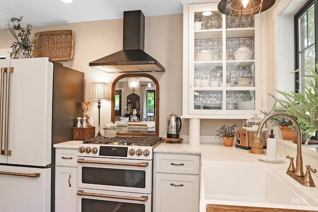 kitchen with sink, white cabinets, white appliances, and wall chimney exhaust hood