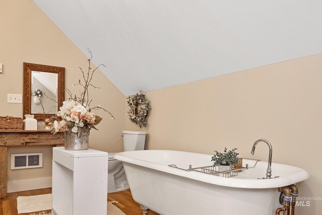 bathroom with a tub to relax in, vaulted ceiling, toilet, and wood-type flooring