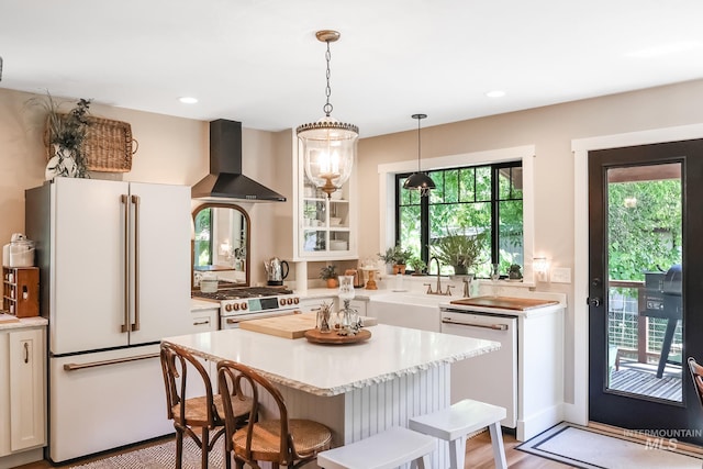 kitchen with a breakfast bar, white cabinets, premium appliances, and wall chimney exhaust hood