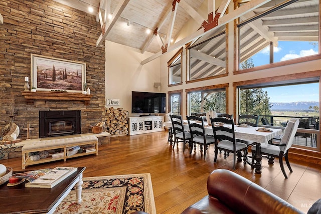 living room featuring beamed ceiling, high vaulted ceiling, and a stone fireplace