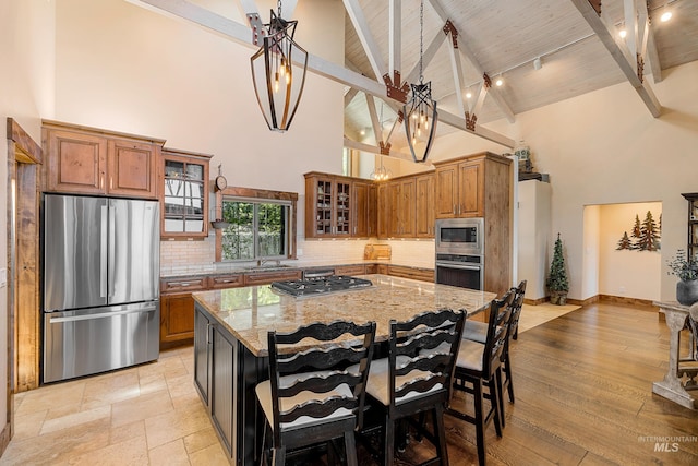 kitchen with light hardwood / wood-style flooring, light stone counters, a kitchen island, high vaulted ceiling, and appliances with stainless steel finishes