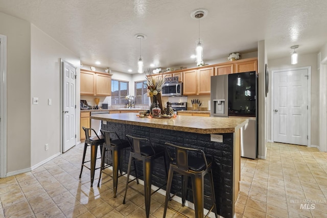 kitchen featuring a kitchen island, a sink, appliances with stainless steel finishes, a textured ceiling, and a kitchen bar