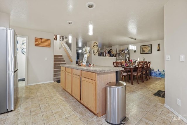 kitchen featuring light brown cabinets, a kitchen island, freestanding refrigerator, light countertops, and hanging light fixtures