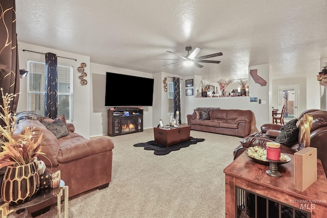 carpeted living room featuring a glass covered fireplace, a textured ceiling, and ceiling fan