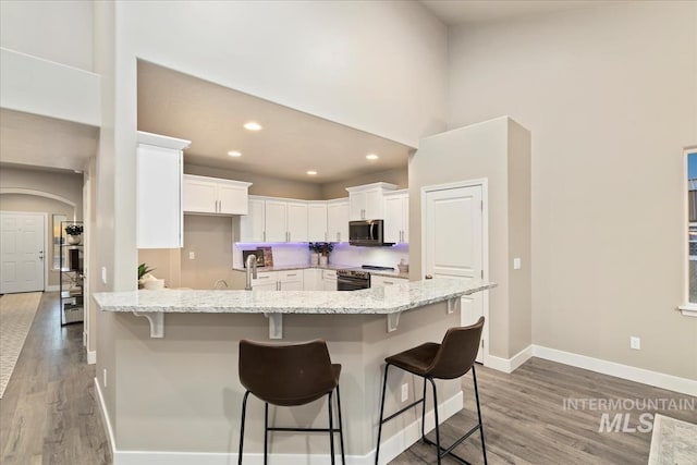 kitchen featuring a breakfast bar, white cabinets, light stone counters, wood-type flooring, and stainless steel appliances