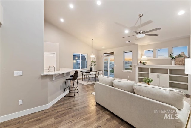 living room with hardwood / wood-style flooring, ceiling fan with notable chandelier, and vaulted ceiling