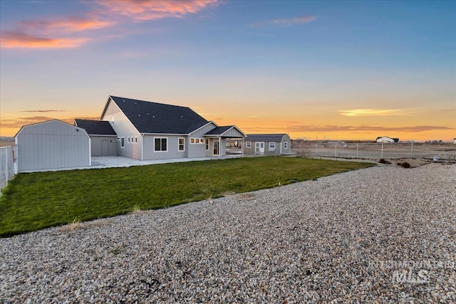 back house at dusk featuring a lawn, a patio area, and a storage shed