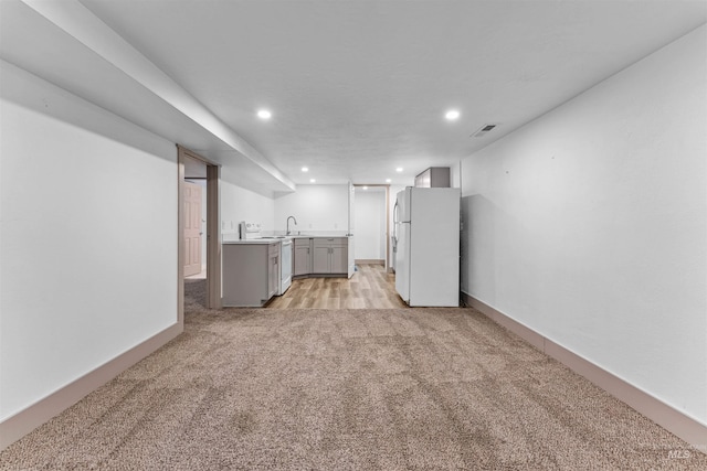 finished basement with visible vents, freestanding refrigerator, recessed lighting, and light colored carpet