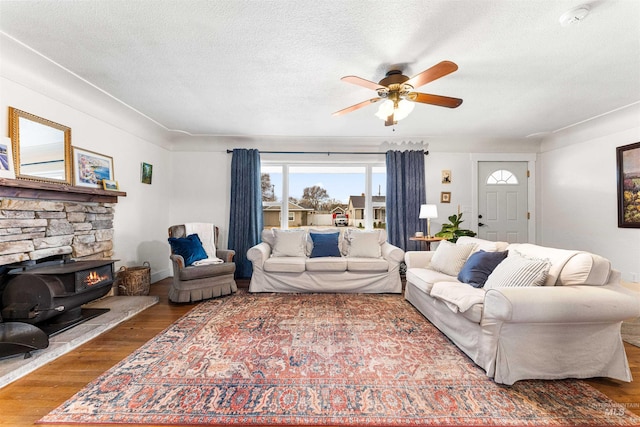 living area with a ceiling fan, a textured ceiling, a fireplace, baseboards, and wood-type flooring
