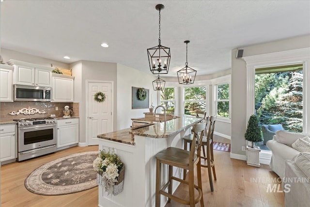 kitchen featuring backsplash, hanging light fixtures, an island with sink, and stainless steel appliances