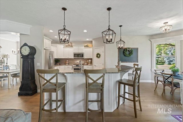 kitchen with white cabinets, decorative light fixtures, stainless steel appliances, and dark stone counters