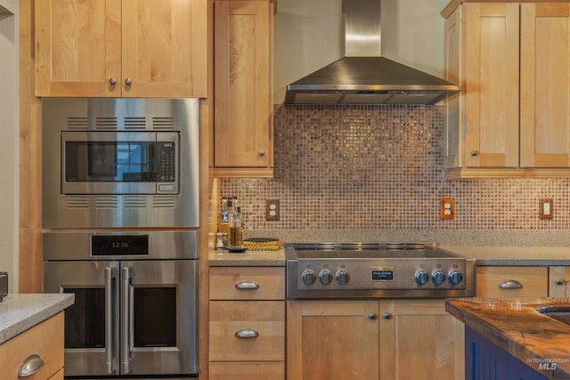 kitchen with butcher block countertops, appliances with stainless steel finishes, wall chimney exhaust hood, and tasteful backsplash