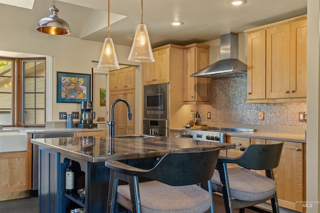 kitchen featuring light brown cabinetry, a center island with sink, sink, and wall chimney range hood