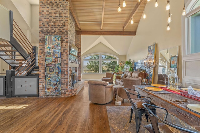 dining area featuring beamed ceiling, a fireplace, a notable chandelier, wood-type flooring, and high vaulted ceiling