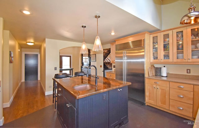 kitchen featuring stainless steel built in refrigerator, pendant lighting, an island with sink, and sink