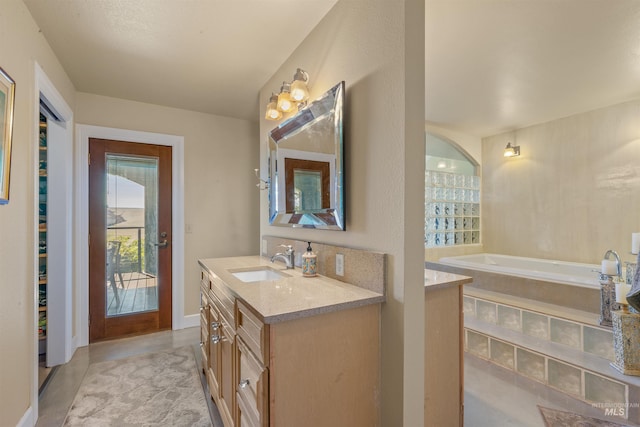 bathroom featuring tile patterned floors, a relaxing tiled tub, and vanity