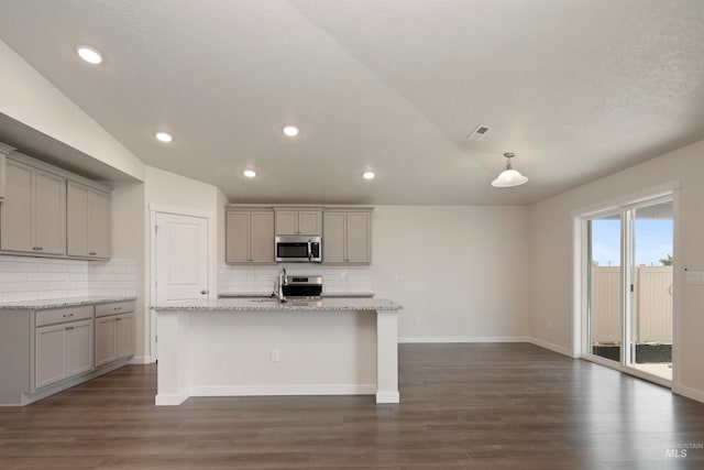 kitchen with light stone counters, dark wood-type flooring, appliances with stainless steel finishes, gray cabinets, and a center island with sink