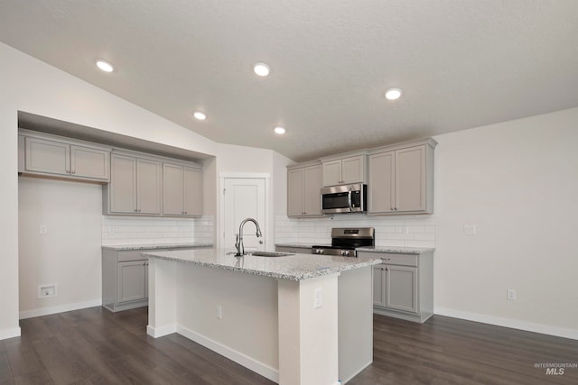 kitchen featuring an island with sink, lofted ceiling, dark hardwood / wood-style floors, stainless steel appliances, and sink