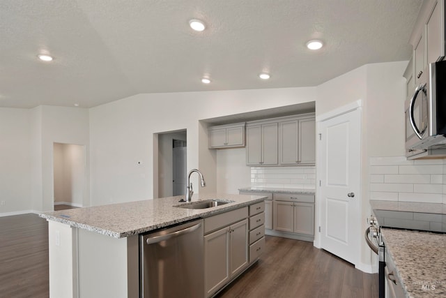 kitchen featuring decorative backsplash, a kitchen island with sink, stainless steel appliances, sink, and vaulted ceiling