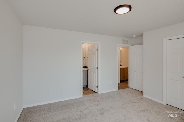 unfurnished bedroom with ensuite bath and light carpet