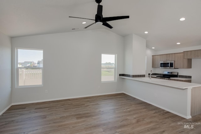 kitchen featuring vaulted ceiling, kitchen peninsula, stainless steel appliances, and light hardwood / wood-style floors